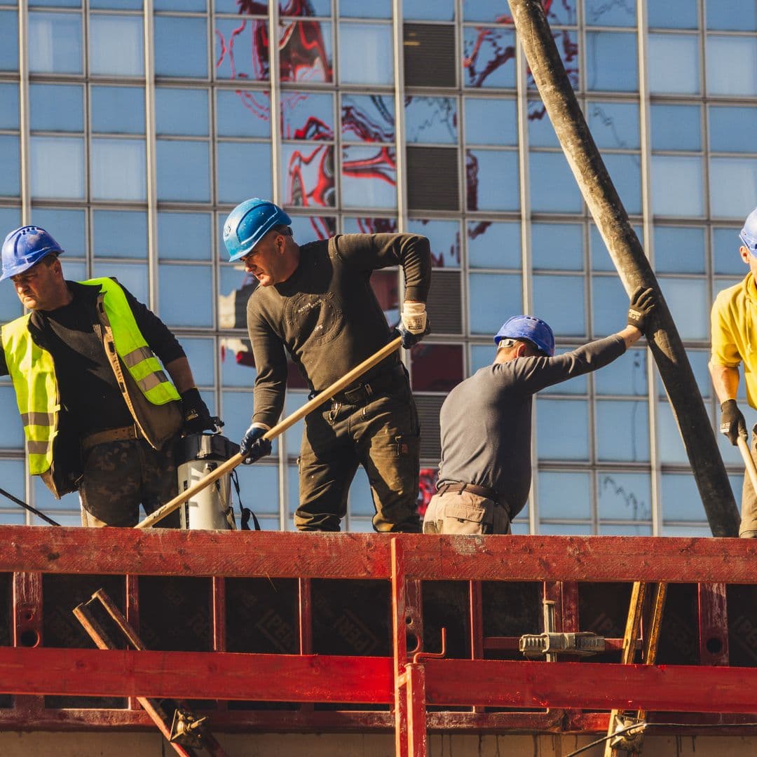Operarios de la construcción con casco y chaleco trabajando en la losa de una obra