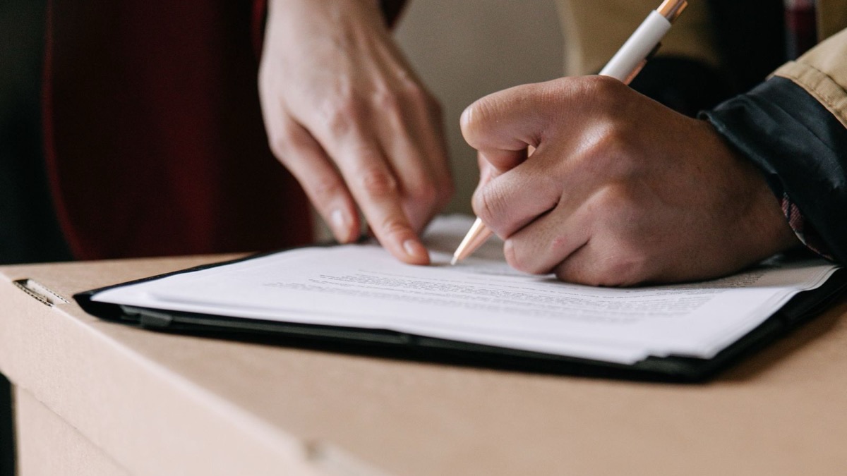 Dos personas firman un contrato de alquiler sobre una caja de mudanza