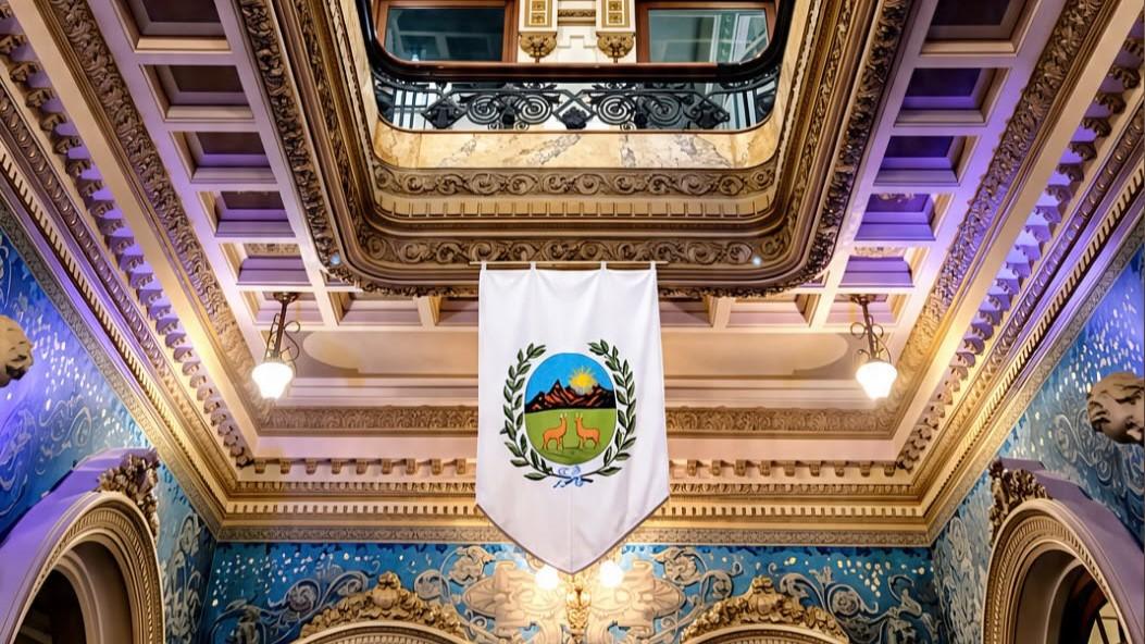 El escudo de San Luis cuelga bajo el cielorraso ornamentado, con relieves dorados y murales azules que distinguen los interiores del Palacio Lagomarsino (Foto IG: @buenosairesarquitectura)