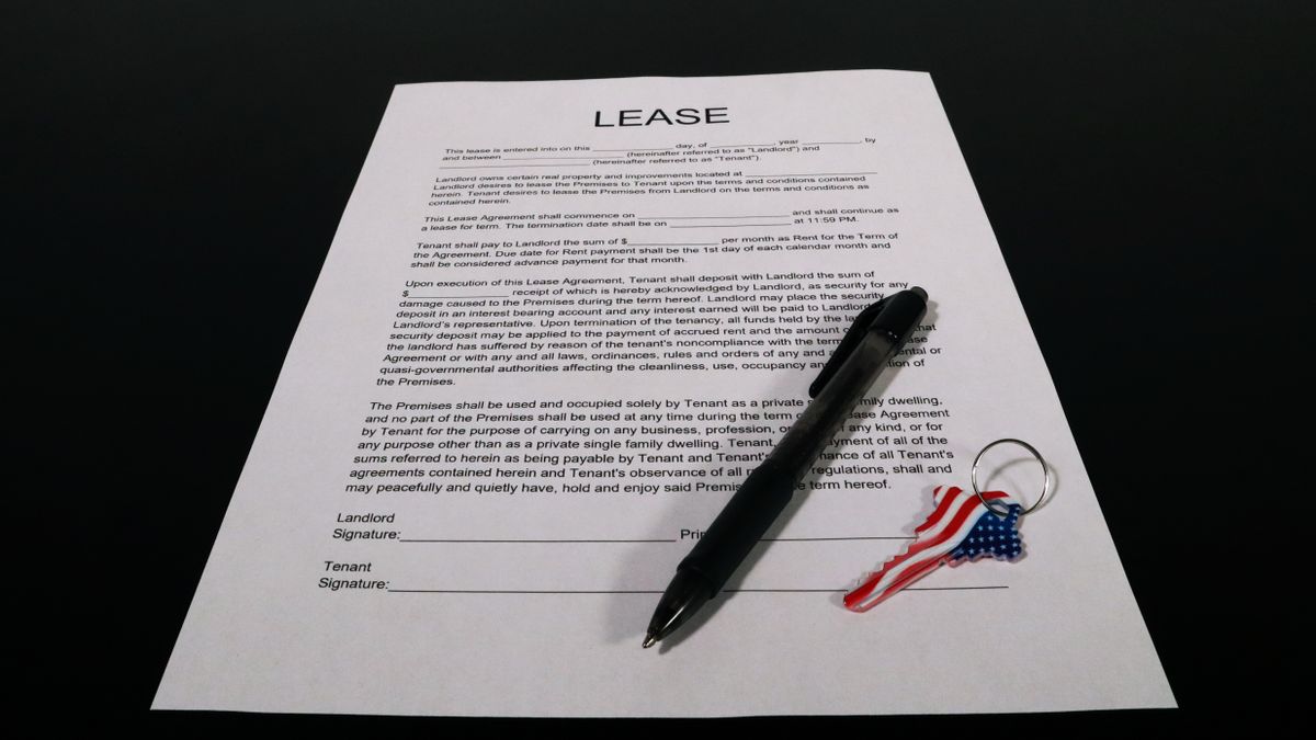 Persona firmando contrato de alquiler con documentación sobre una mesa