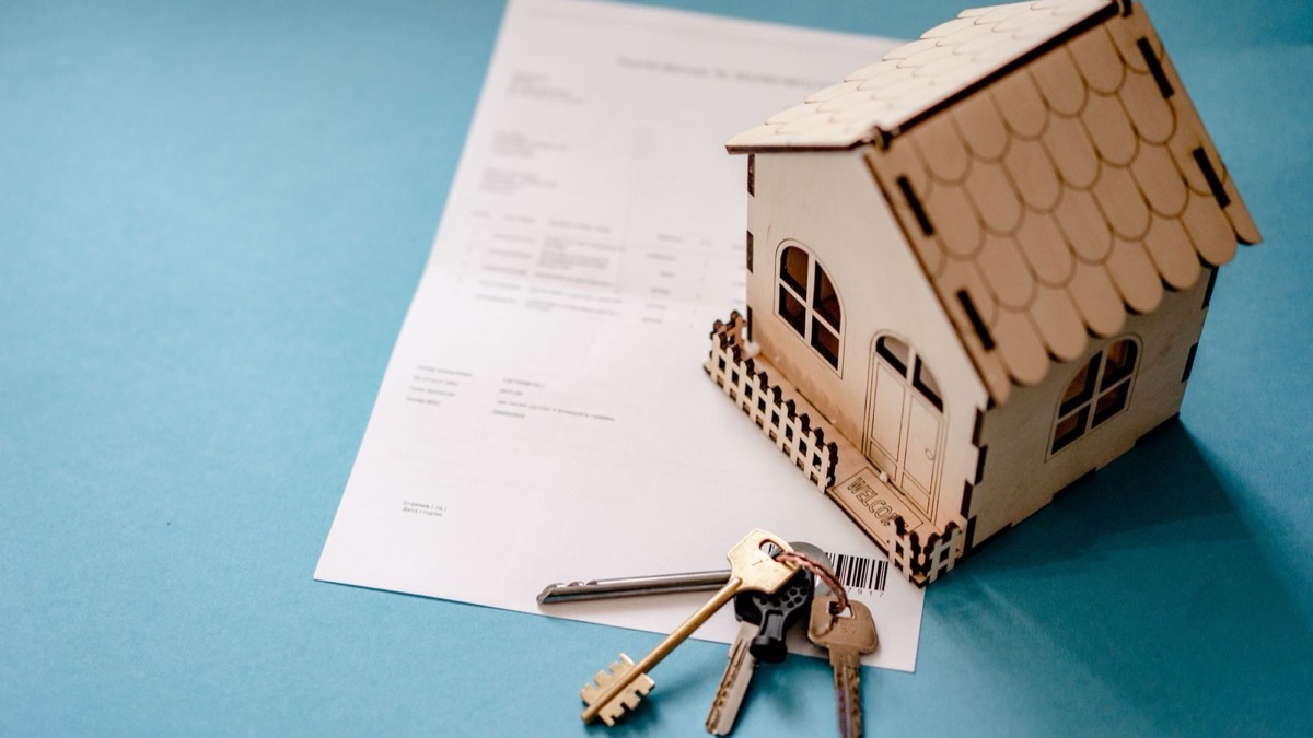 Llaves de un departamento sobre un contrato de alquiler, junto a una casa en miniatura